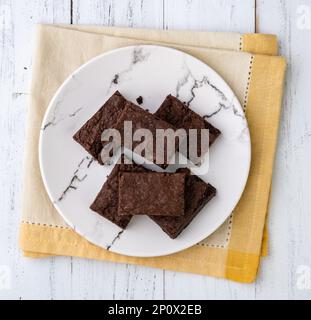 Brownies auf einem Teller mit Schokoladenstückchen und Walnüssen auf einem weißen Holztisch. Stockfoto