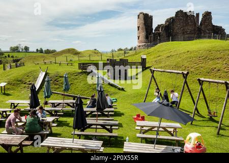 Die Menschen sitzen in einem Café und Spielplatz vor den Ruinen von Brough Castle aus dem 11. Jahrhundert, die sich auf der römischen Festung von Verteris, Brough Cumbria, befinden Stockfoto