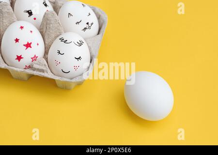 Osterkarte. Weiße Eier, mit einem Lächeln bemalt und eine zum Schreiben leer gelassen. Gelber Hintergrund. Draufsicht mit Kopierbereich. Frohe Feiertage. Stockfoto