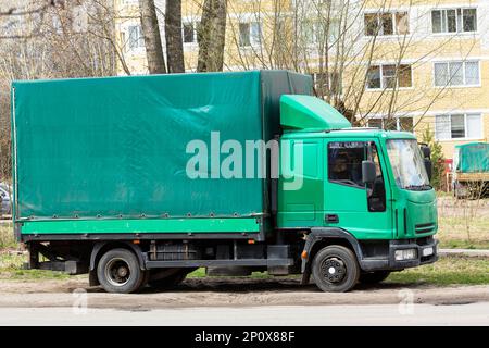 Verkehr, Lieferung, ein kleiner grüner Logistikwagen auf der Straße vor dem Hintergrund von Wohngebäuden. Stockfoto