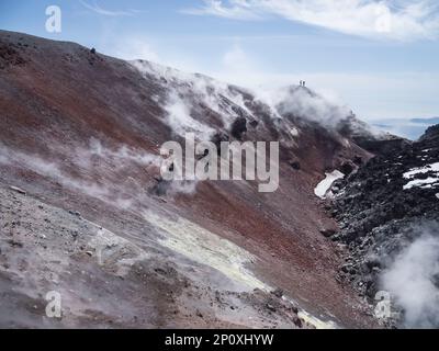 Silhouette von Männern beim Wandern in der Caldera des Stratovulkans Avachinsky, auch bekannt als Vulkan Avacha. Rucksacktouristen bewegen sich auf Felsen hinter Dampf von Stockfoto