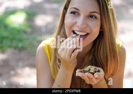 Nahaufnahme einer attraktiven gesunden Frau, die Paranüsse im Park isst Stockfoto