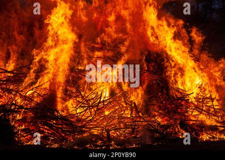 Ein großer Haufen Holzstäbchen auf einem grasbedeckten Feld, umgeben von einer Decke aus Flammen Stockfoto