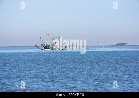 Ein Fischerboot, das auf dem Ozean mit einem Leuchtturm im Hintergrund schwimmt Stockfoto