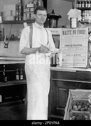 Innenraum des Stores. 'Reste No Food', 1917 oder 1918. Poster zur Kriegszeit: „Haushaltsabfall ca. 700 Millionen Dollar... Lebensmittel werden verschwendet, wenn etwas essbares in den Mülleimer gelangt oder wegen mangelnder ordnungsgemäßer Handhabung verderben darf...[wenn] wir mehr essen, als unser Körper für Wachstum und Reparatur und für die Energieversorgung unserer Arbeit benötigt... demonstrieren Sie Thrift in Ihrem Zuhause - Sparen statt ausgeben, Ihr Sozialstandard... USA Landwirtschaftsministerium“. Stockfoto