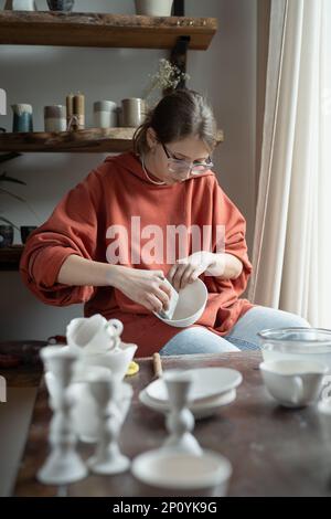 Fokussierte, konzentrierte Keramikarbeiterin, die in einem Handwerksgeschäft einen Tonartikel hält. Stockfoto