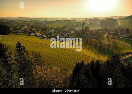 Wunderbarer Blick aus der Vogelperspektive auf die abendliche Atmosphäre über Zell am Pettenfirst, Österreich, wo die alte Kirche und andere Gebäude sehr lange Schatten werfen Stockfoto