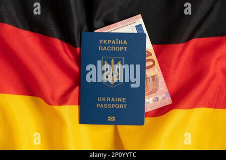 Die Flagge Deutschlands in der Mitte liegt ein biometrischer ausländischer Pass eines Ukrainers und zehn Euro, die nach Deutschland migrieren Stockfoto