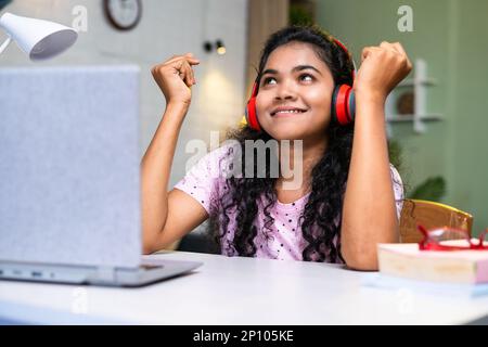 Mädchen, die Musik über kabellose Kopfhörer von einem Notebook aus hört, während sie zu Hause am Schreibtisch lernt – Konzept von Entspannung, Stressabbau und Technologie Stockfoto