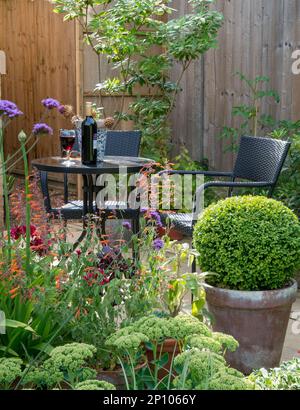 Kleiner Tisch und Stühle mit einer Flasche Rotwein und Glas in einem Garten Stockfoto