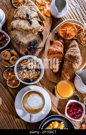 Frühstück mit Kaffee, Orangensaft, Rührei, Müsli, Pfannkuchen und Croissants. Stockfoto