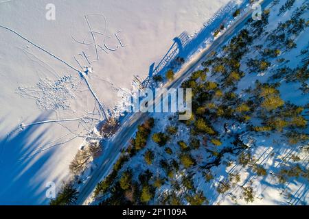 Eine malerische Winterlandschaft mit einer kurvenreichen Straße durch ein schneebedecktes Feld mit dem Wort Frieden auf Schnee Stockfoto