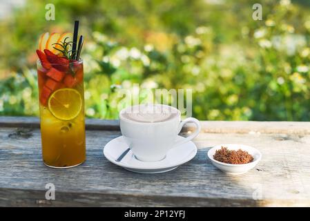 Glas grüner tropischer Tee mit Limette, Orange, Wassermelone und Apfel auf Grün und Cappuccino mit braunem Zucker im Sommer Stockfoto