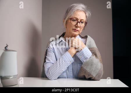 Die bescheidene alte Dame sitzt allein an einem Tisch Stockfoto