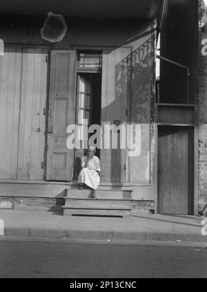 Blick von der anderen Straßenseite auf eine Frau, die auf den Stufen sitzt, New Orleans, zwischen 1920 und 1926 Uhr. Stockfoto