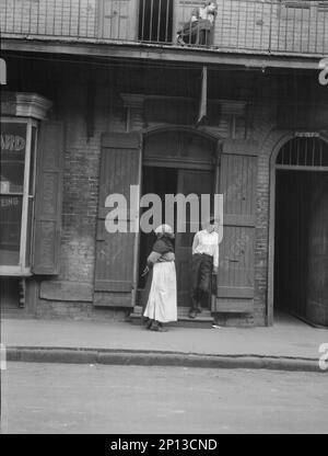 Blick von der anderen Straßenseite auf einen Mann und eine Frau, die zwischen 1920 und 1926 Uhr an einer Tür stehen und auf dem Balkon über dem neuen Platz sitzen. Stockfoto