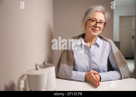 Eine ziemlich ältere Frau sitzt zu Hause am Küchentisch Stockfoto