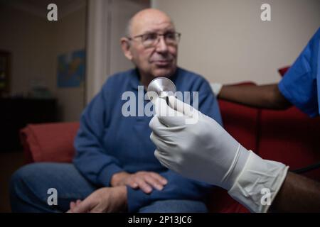 Nahaufnahme einer Arzthandhaltung eines Stethoskops bei der ärztlichen Untersuchung eines älteren Patienten. Stockfoto