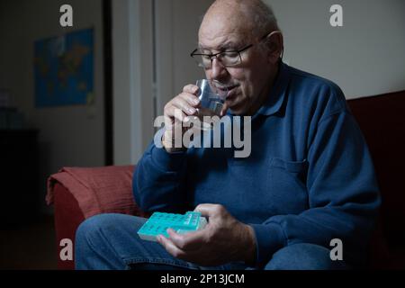 Ein älterer Mann nimmt Medikamente von seinem Pillen Organisator und trinkt Wasser, häusliche Gesundheitsversorgung Stockfoto