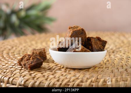 Kithul Jaggery und Treakel natürlicher Süßstoff in weißer Schüssel auf traditioneller Weidenschale. Schließen. Alternativer Zucker. Essen mit niedrigem GI-Wert. Superfood. Stockfoto