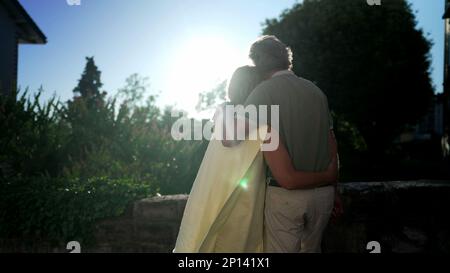 Ein fröhliches Seniorenpaar umarmt es, draußen zu stehen und die Sonne zu sehen. Zarter Moment zwischen einem älteren verheirateten Mann und einer Frau, die den Arm um den Vater herum hat Stockfoto