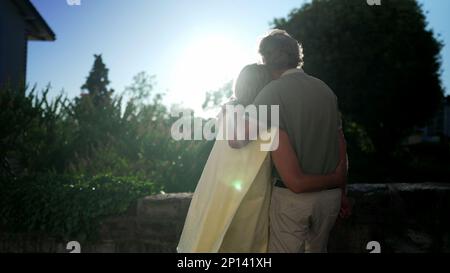 Ein fröhliches Seniorenpaar umarmt es, draußen zu stehen und die Sonne zu sehen. Zarter Moment zwischen einem älteren verheirateten Mann und einer Frau, die den Arm um den Vater herum hat Stockfoto