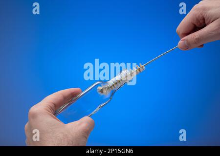 Reinigen Sie eine leere Glasflasche mit einer kleinen Drahtbürste. Männliche Hand, die sie hält. Nahaufnahme des Studios, isoliert auf blauem Hintergrund. Stockfoto