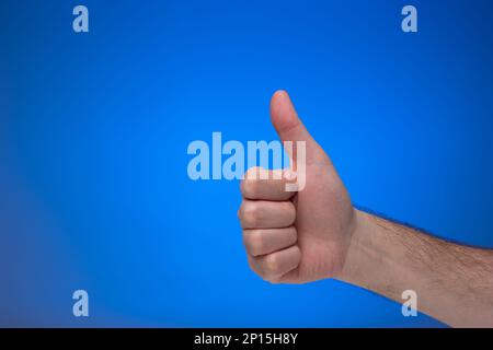 Der Daumen ist oben, wie eine Geste von einer weißen männlichen Hand. Nahaufnahme des Studios, isoliert auf blauem Hintergrund. Stockfoto