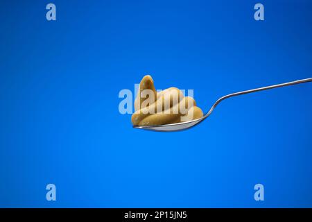 Senfpaste auf einem kleinen silbernen Löffel Nahaufnahme Studio, isoliert auf blauem Hintergrund. Stockfoto