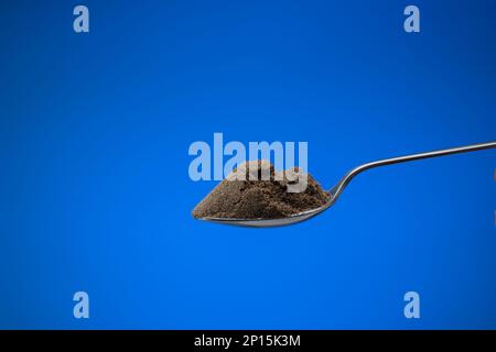 Fein gemahlenes schwarzes Pfefferpulver in einem kleinen silbernen Löffel. Nahaufnahme des Studios, isoliert auf blauem Hintergrund. Stockfoto