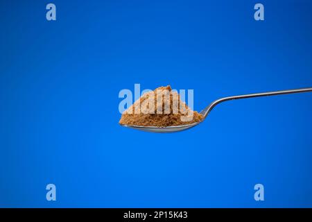 Fein gemahlenes Gewürzpulver in einem kleinen silbernen Löffel. Nahaufnahme des Studios, isoliert auf blauem Hintergrund. Stockfoto