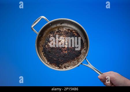 Dreckige, ölig verbrannte Bratpfanne aus Metall, die von Männern in der Hand gehalten wird. Stockfoto