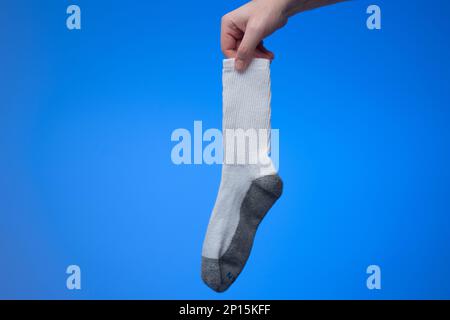 Eine trockene und saubere Baumwollsocke, die von einem weißen Mann in der Hand gehalten wird. Nahaufnahme des Studios, isoliert auf blauem Hintergrund. Stockfoto