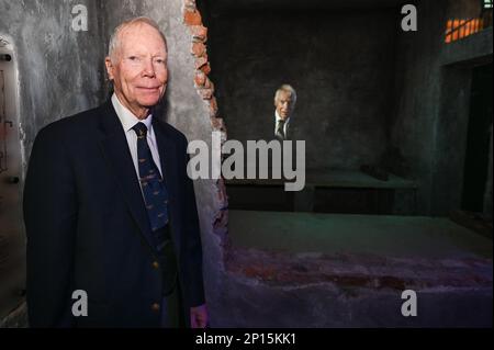 US-Rentner Navy Rear ADM. Robert „Shu“ Shumaker lässt sich während der großen Eröffnung der Hanoi Hilton Vietnam-Ausstellung im American Heritage Museum, Hudson, Mass, neben der Originalzelle aus dem Gefängnis von Hỏa Lò fotografieren. Februar 11. Shumaker, ein ehemaliger Kriegsgefangener, wurde am 11. Februar 1965 abgeschossen. Er verbrachte acht Jahre in Gefangenschaft, drei davon in Einzelhaft. Stockfoto