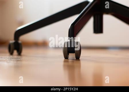 Schwarzer Bürostuhl aus Metall mit drehbaren Rädern auf Holzfußboden, geringe Tiefenschärfe, niemand. Stockfoto