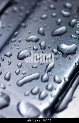 Große Wassertröpfchen, die sich auf einem blau getönten Edelstahlspüle in der Nahaufnahme angesammelt haben. Stockfoto