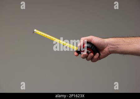 Weiße männliche Hand, die ein Maßbandlineal hält, isoliert auf grauem Hintergrund. Stockfoto