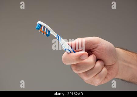 Weiße männliche Hand, die eine gebrauchte Zahnbürste hält, isoliert auf grauem Hintergrund. Stockfoto