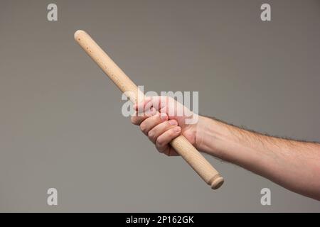 Weiße männliche Hand, die einen langen hölzernen Rollstift hält, isoliert auf grauem Hintergrund. Stockfoto