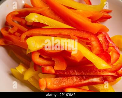 Streifen von geschnittenen roten Orange- und gelben Gemüsepaprika, die in Nahaufnahmen zusammengefasst sind. Stockfoto