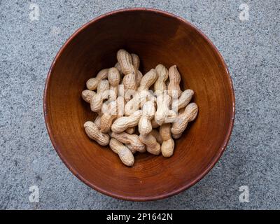 Gruppe ungeschälter Erdnüsse in einer braunen Holzschüssel, Nahaufnahme von oben. Stockfoto