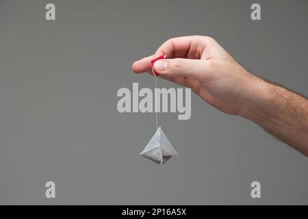 Weiße männliche Hand, die einen Tee schlecht hält, isoliert auf grauem Hintergrund. Stockfoto