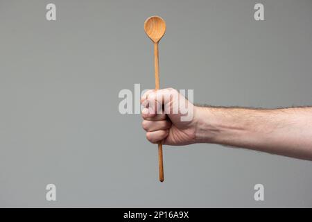 Weiße männliche Hand mit einem Holzlöffel Nahaufnahme isoliert auf grauem Hintergrund. Stockfoto