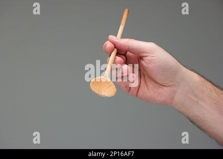 Weiße männliche Hand mit einem Holzlöffel Nahaufnahme isoliert auf grauem Hintergrund. Stockfoto