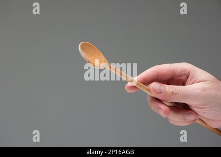 Weiße männliche Hand mit einem Holzlöffel Nahaufnahme isoliert auf grauem Hintergrund. Stockfoto