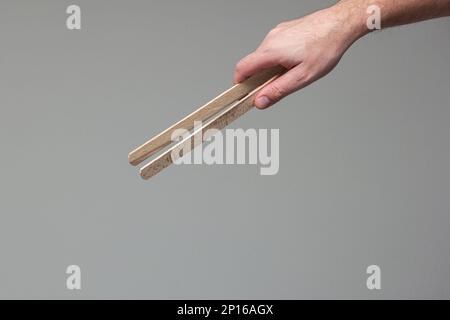 Weiße männliche Hand mit einer hölzernen zange Nahaufnahme isoliert auf grauem Hintergrund. Stockfoto