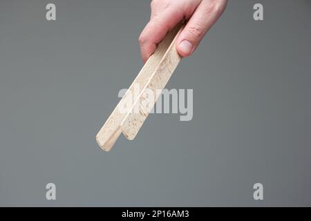 Weiße männliche Hand mit einer hölzernen zange Nahaufnahme isoliert auf grauem Hintergrund. Stockfoto