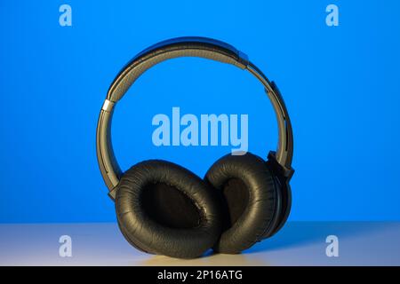 Allgemeiner schwarzer kabelloser Bluetooth-Kopfhörer, isoliert auf blauem Hintergrund. Stockfoto