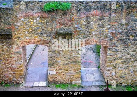 Blick aus dem hohen Winkel auf die dicke Steinmauer mit zwei Bogentüren. Stockfoto
