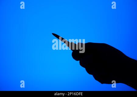 Messerstechergesten-Silhouette schwarz auf blauem Hintergrund, Studioaufnahme unerkennbar. Stockfoto